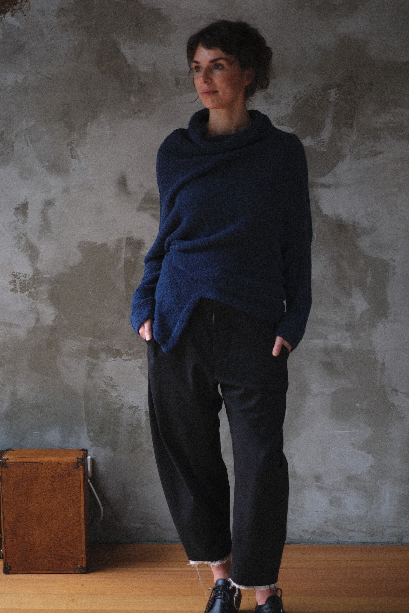 Woman wearing a blue knitted sweater with orange shoulder stitch detail against a textured wall.