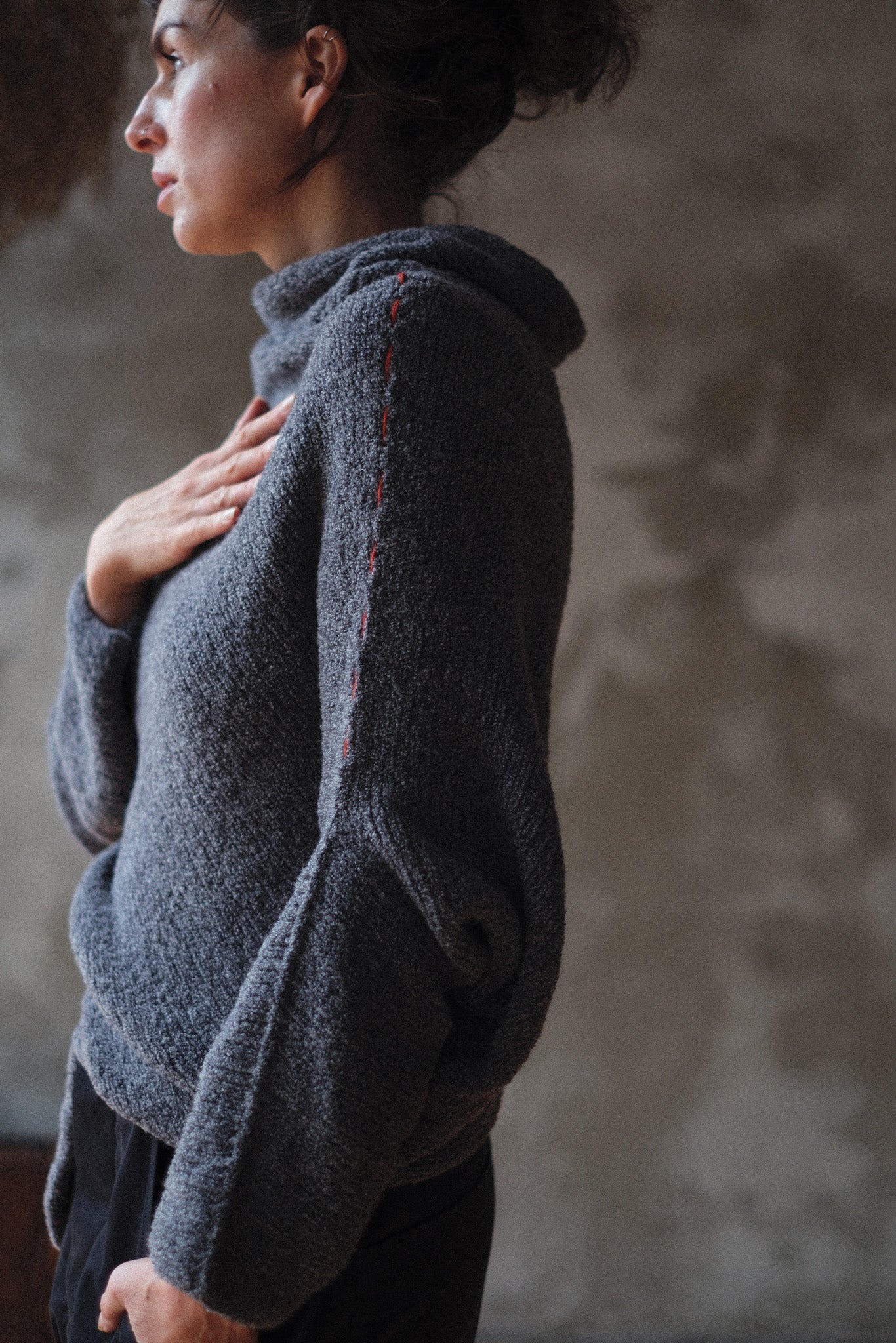 Woman wearing a textured gray sweater with orange shoulder seam detail against a neutral background