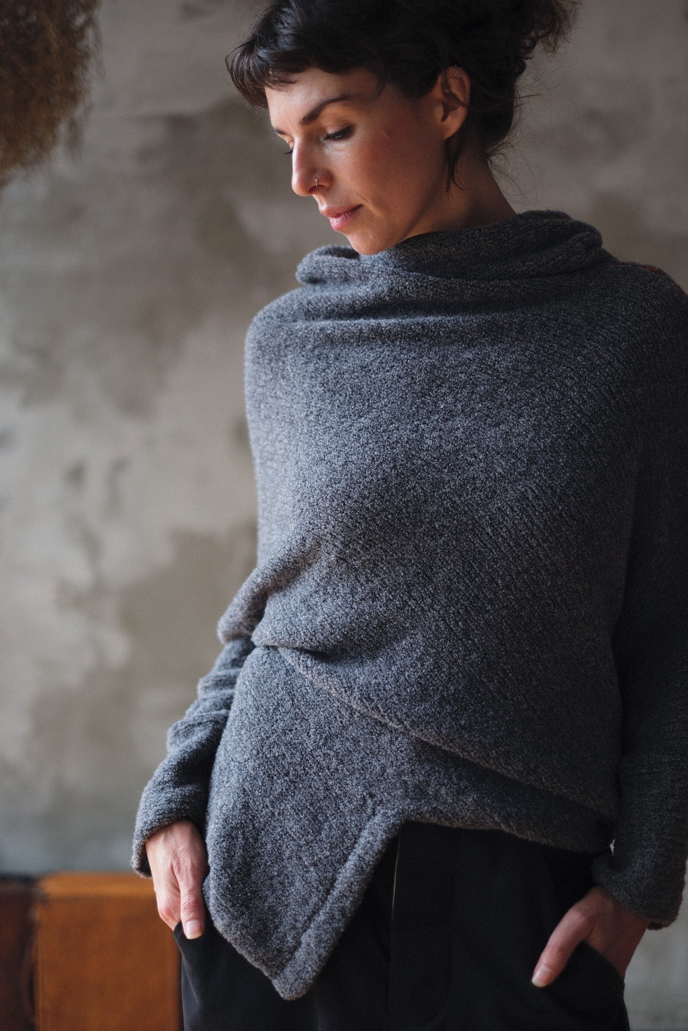 Woman wearing a textured gray sweater with orange shoulder seam detail against a neutral background
