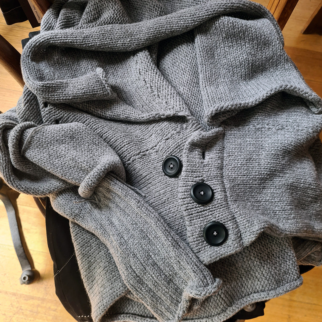 Soft grey knitted cardigan with black buttons on a chair