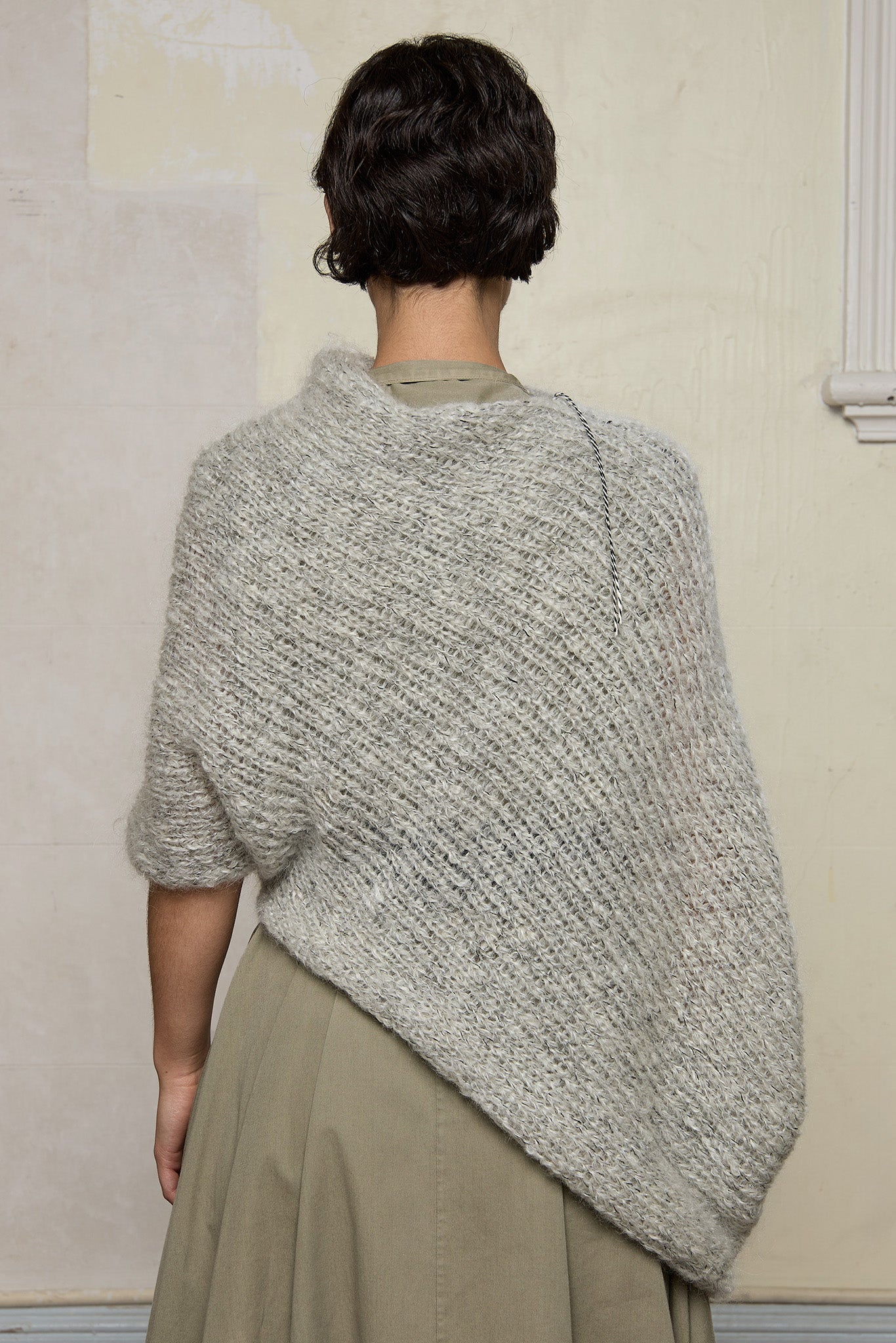 Back view of model wearing mohair cocoon, an asymmetric poncho in a white flecked colourway