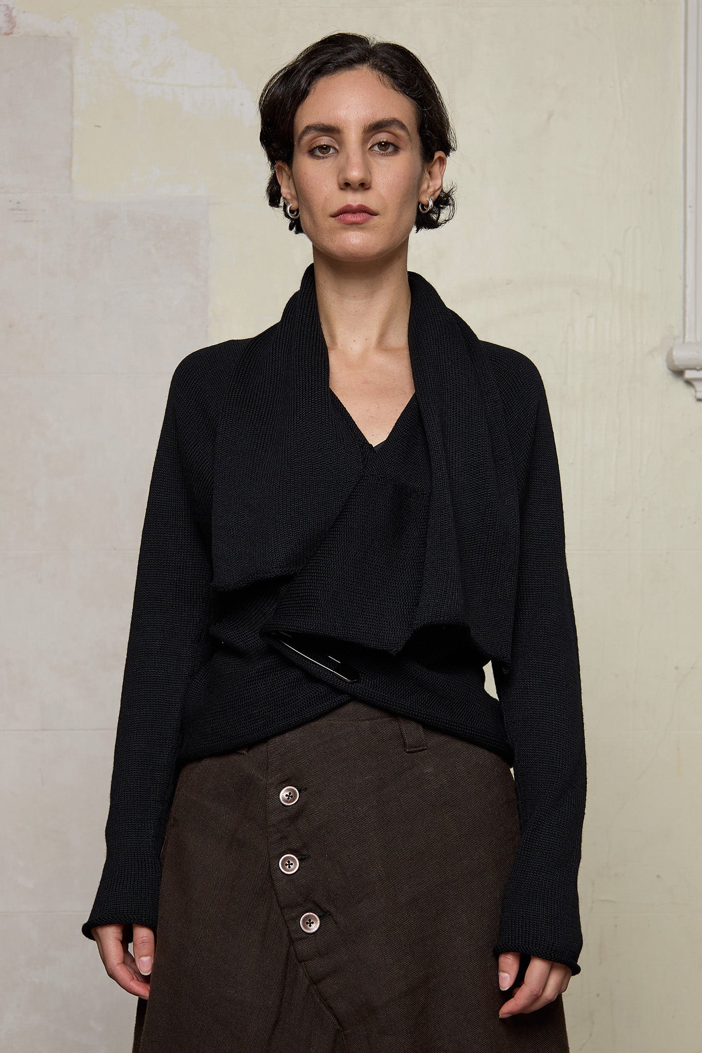 Model wears a knitted shawl collared cardigan upside down and pinned at the waist in a black colourway.  Cardigan is designed and knitted in  Melbourne by Wendy Voon knits.
