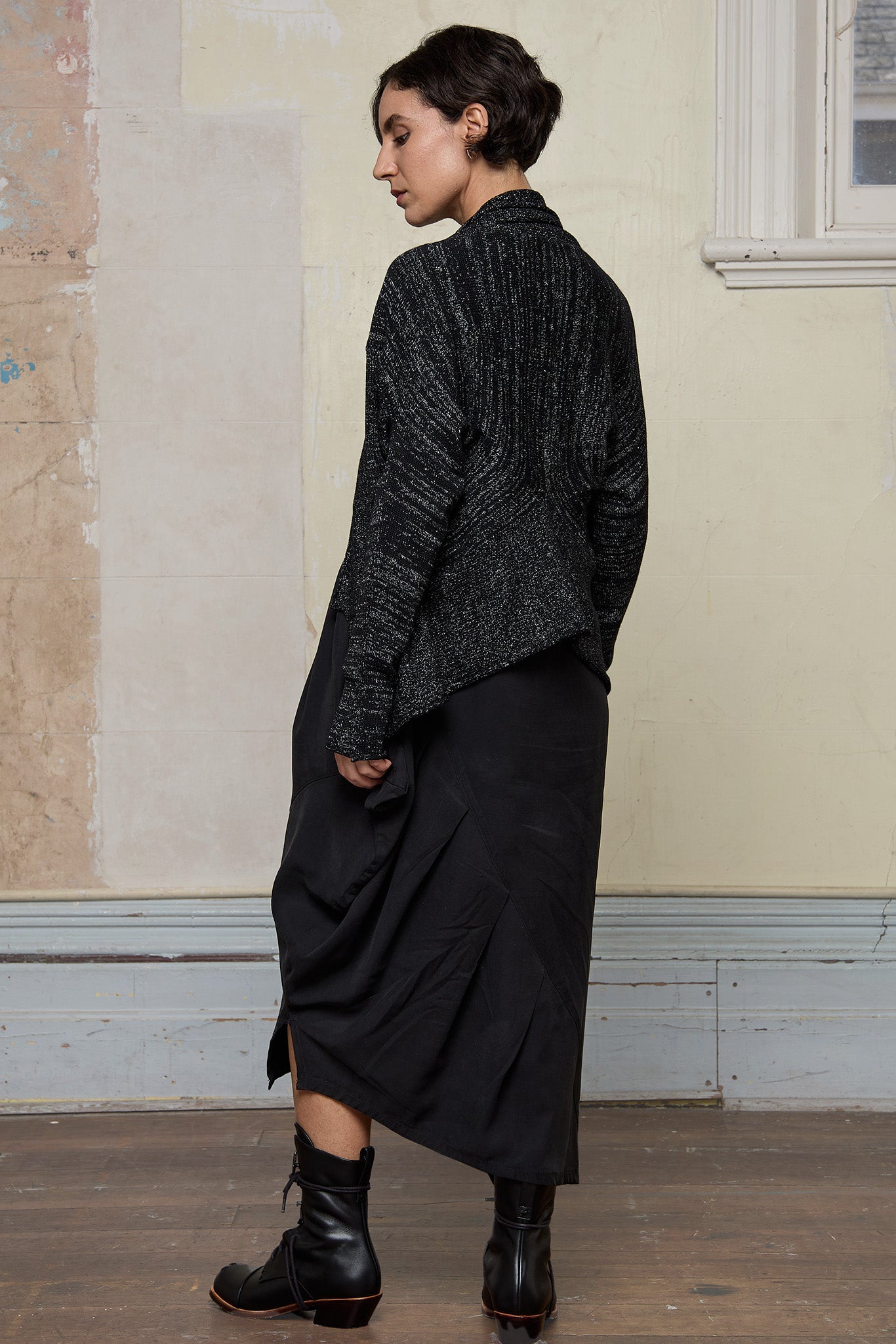 Back view of model wearing a black with white flecks shawl collared cardigan.