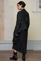 Back view of model wearing a black with white flecks shawl collared cardigan.