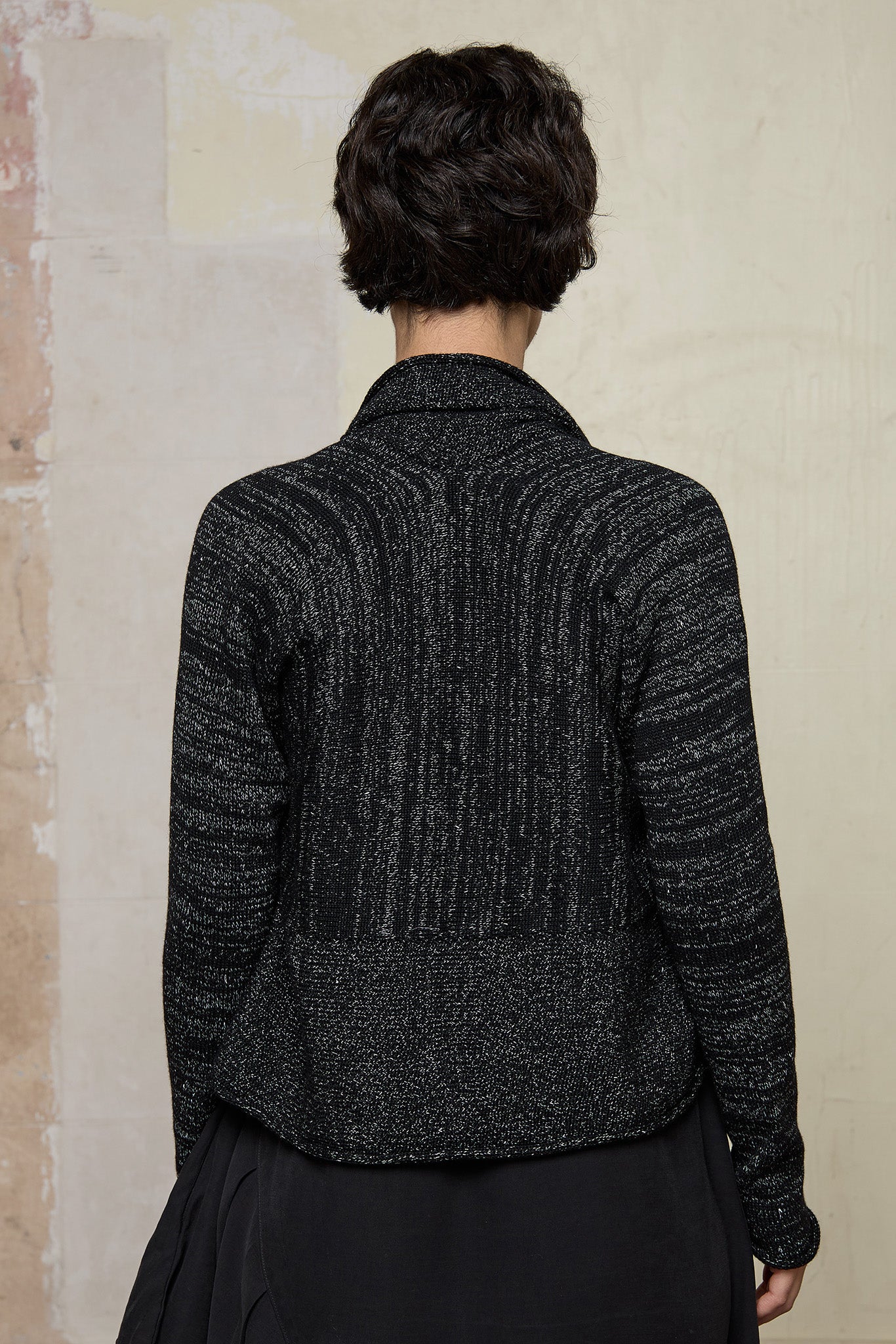 Back view of model wearing a black with white flecks shawl collared cardigan upside down.
