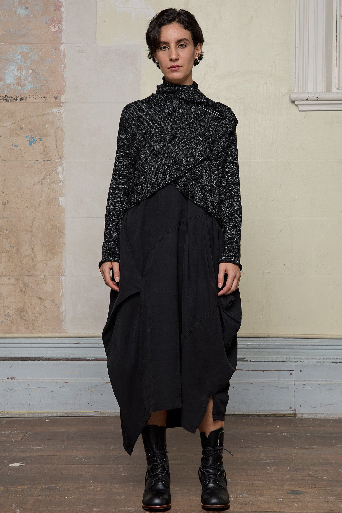 Model wears a black with white flecks shawl collared cardigan upside down, fastened high at the neck with a safety pin.