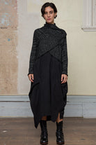 Model wears a black with white flecks shawl collared cardigan upside down, fastened high at the neck with a safety pin.