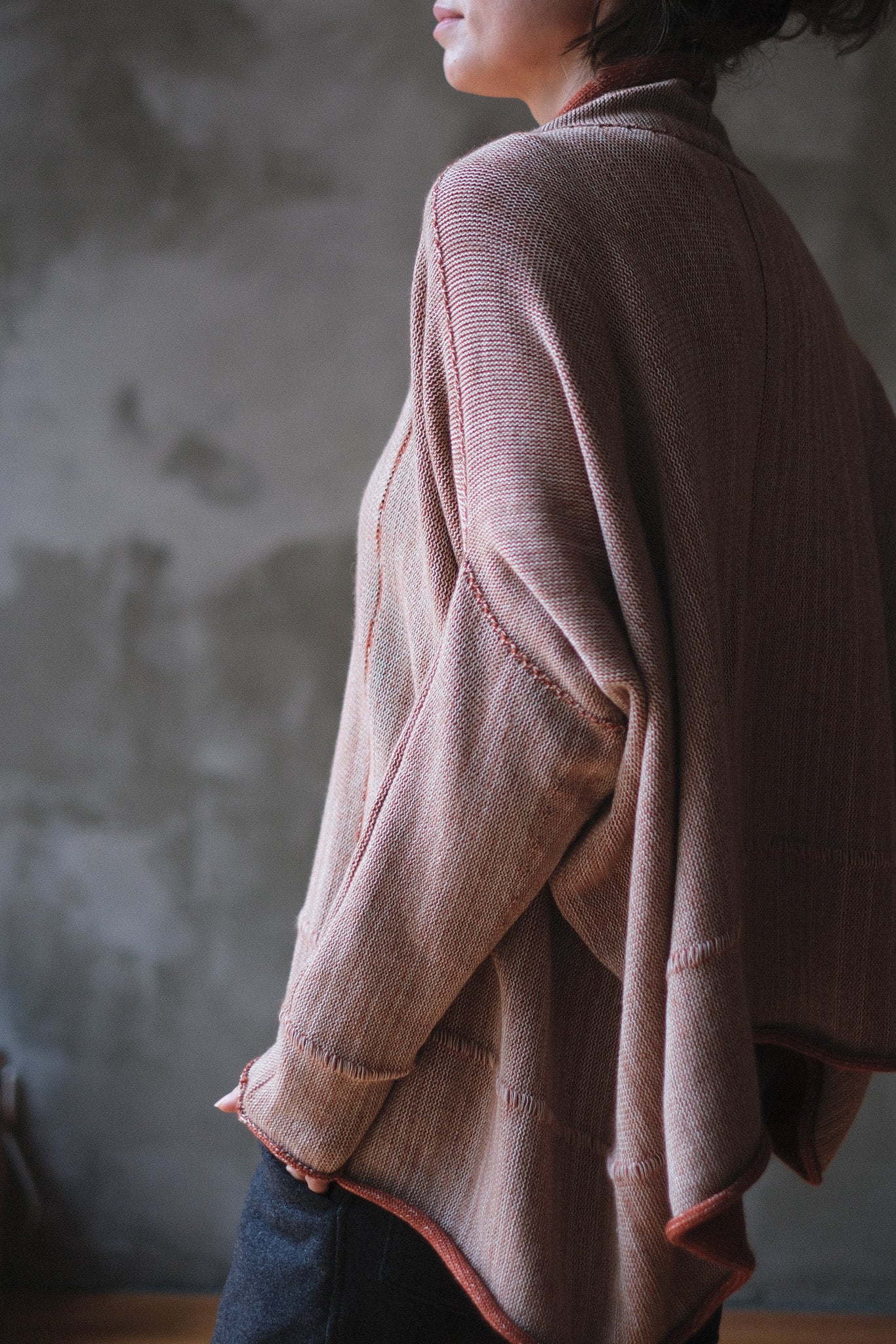 A person shown from the side wearing a loose, draped knit jumper with fawn and terracotta melange colourway (terracotta jumper worn inside out).