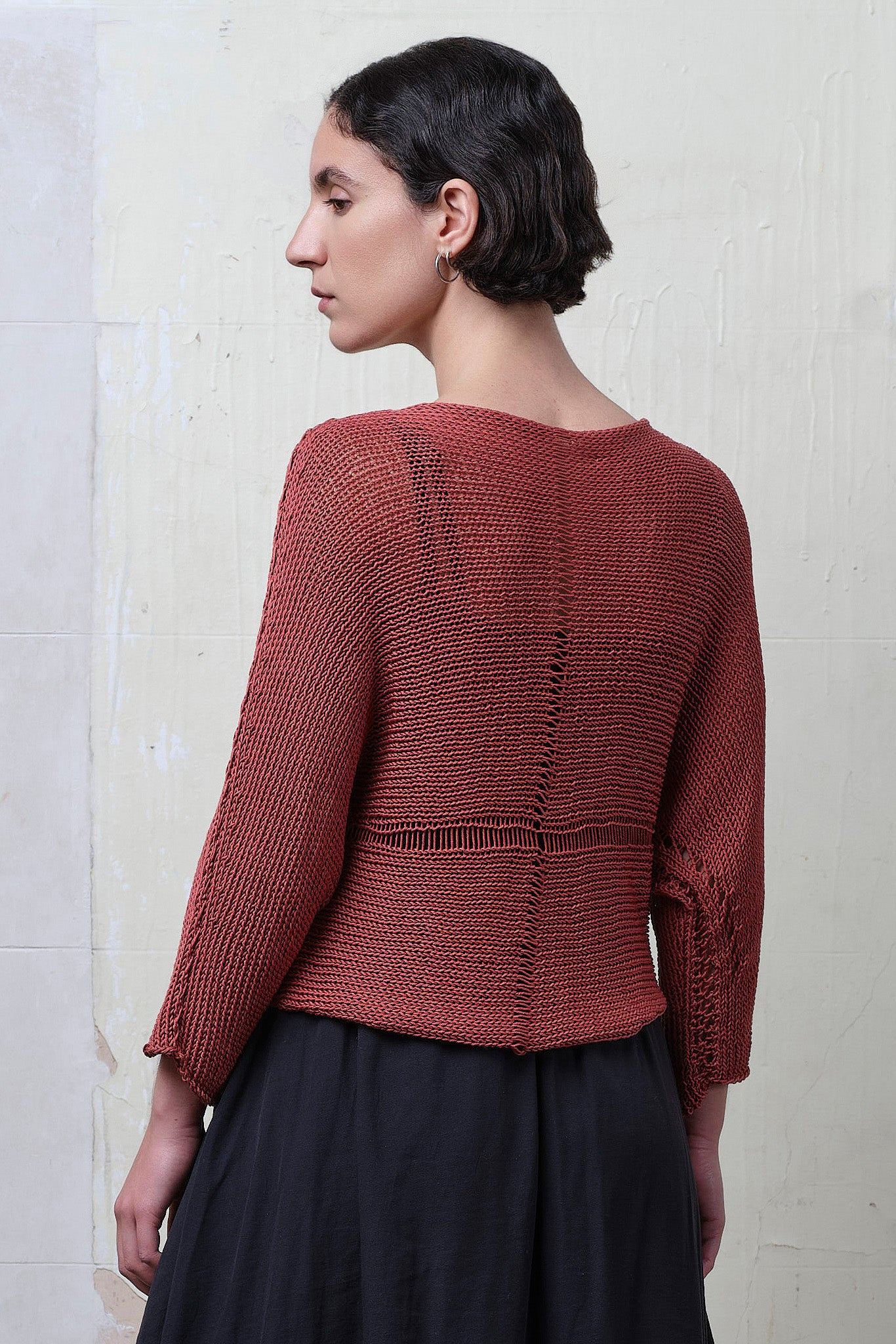 Back 3/4 view of model wearing Cotton Batwing  in coral colourway, featuring large stitch details,  designed by Wendy Voon knits.