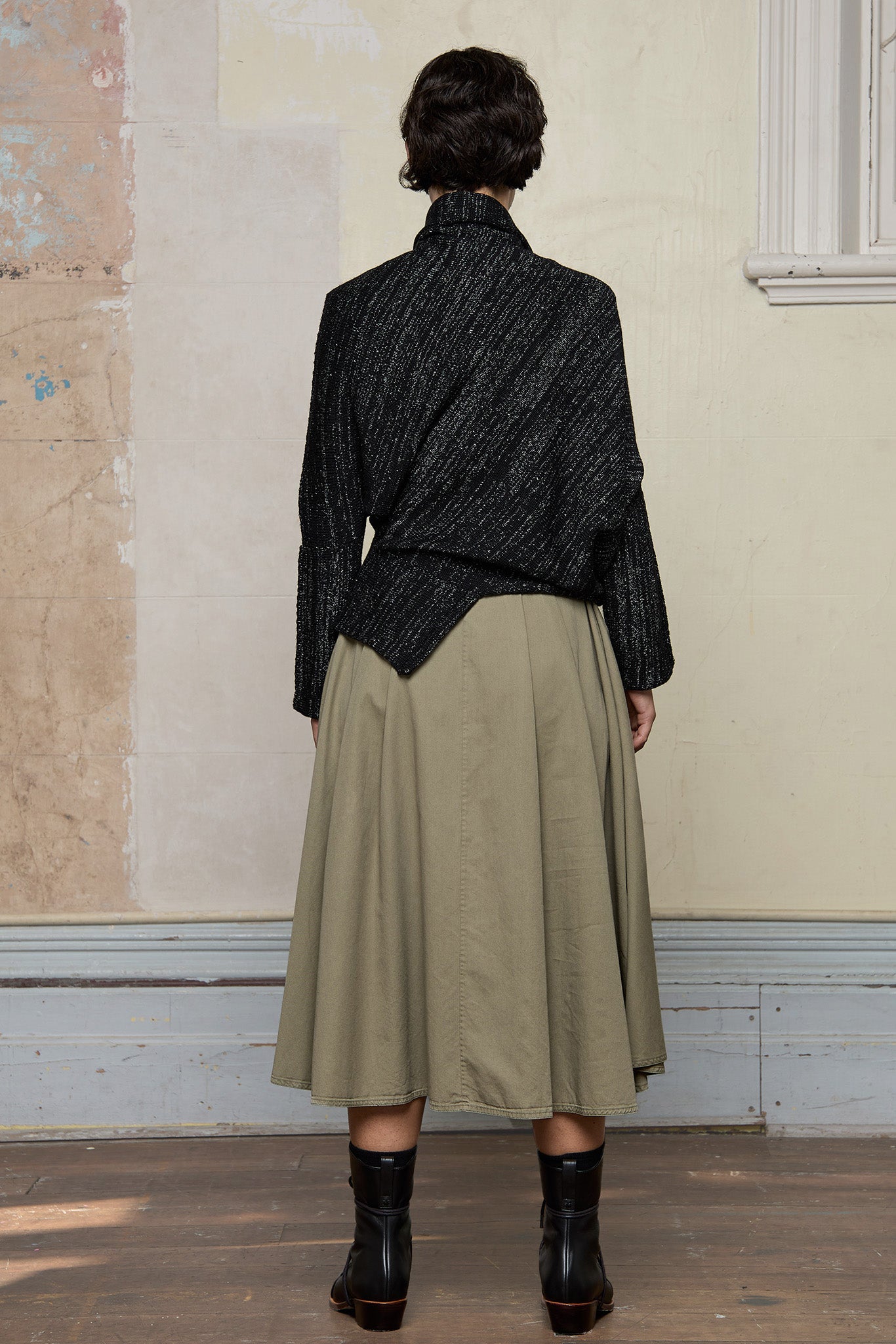 Full body back view of Bias jumper, a design by Wendy Voon knits in a black flecked with white merino wool and linen/cotton blend fabric.