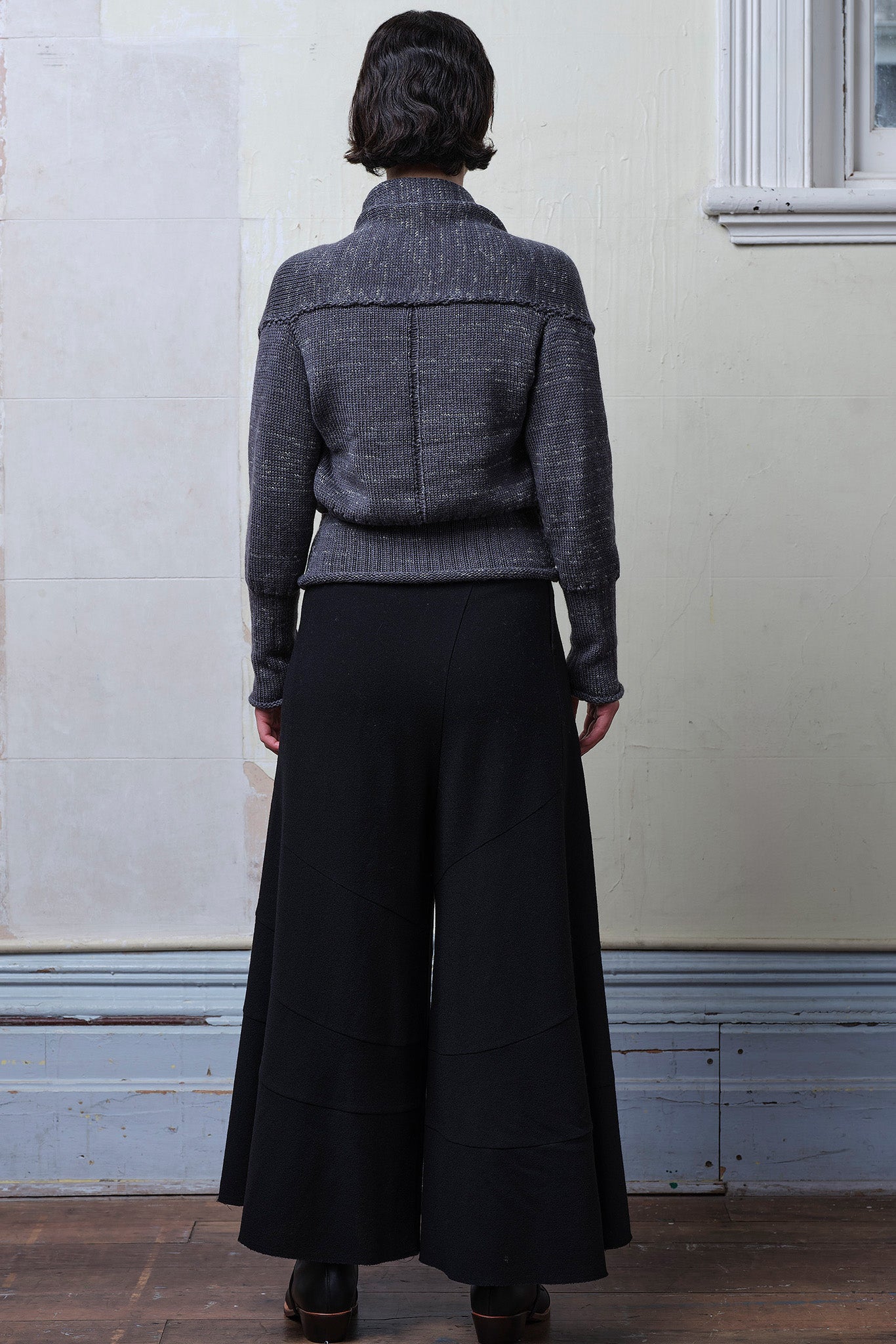 Back full body view of model wearing a chunky knit wool ruched cardigan in a grey with white flecked colourway.