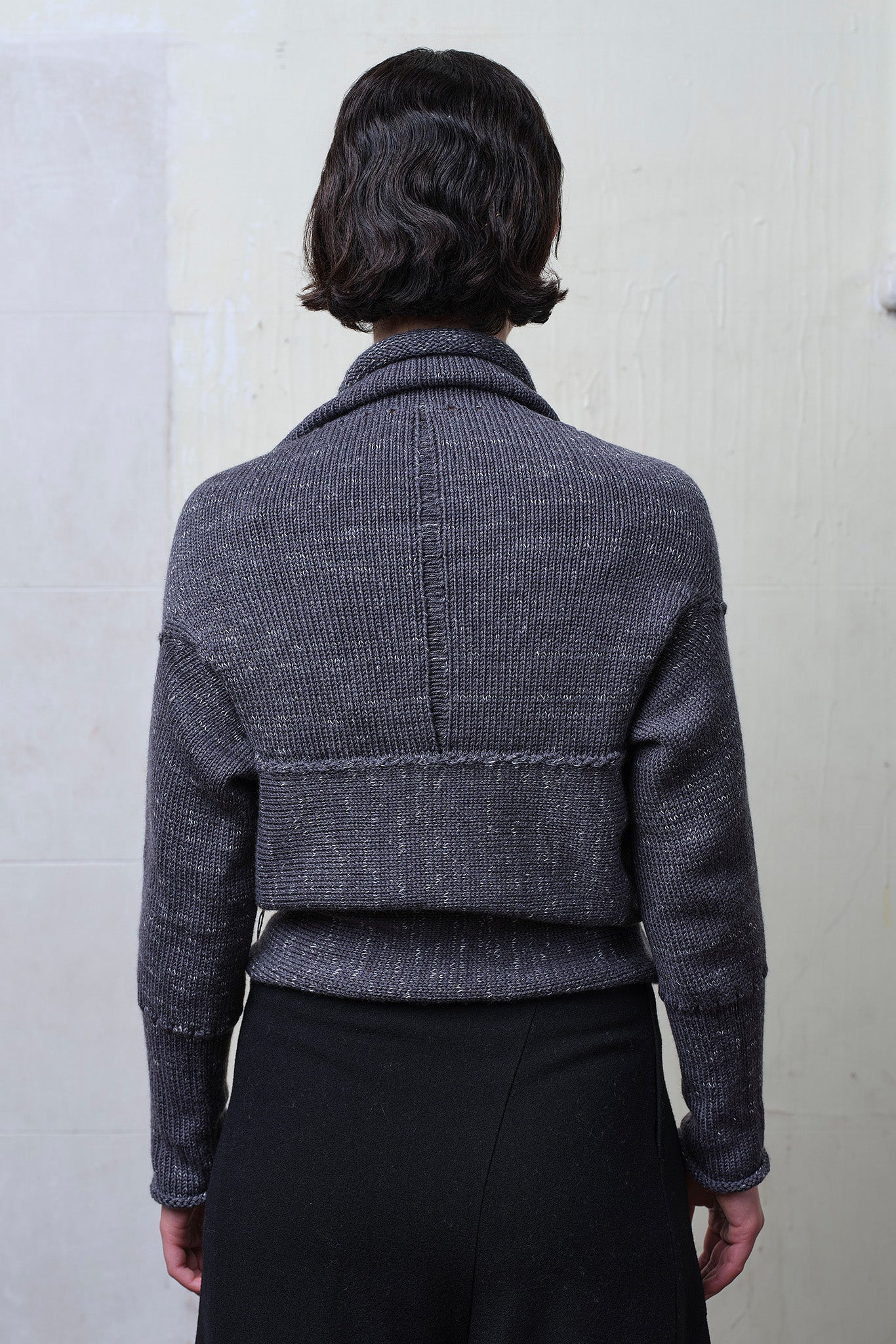 Back view of model wearing a chunky knit wool ruched cardigan upside down, in a grey with white flecked colourway.