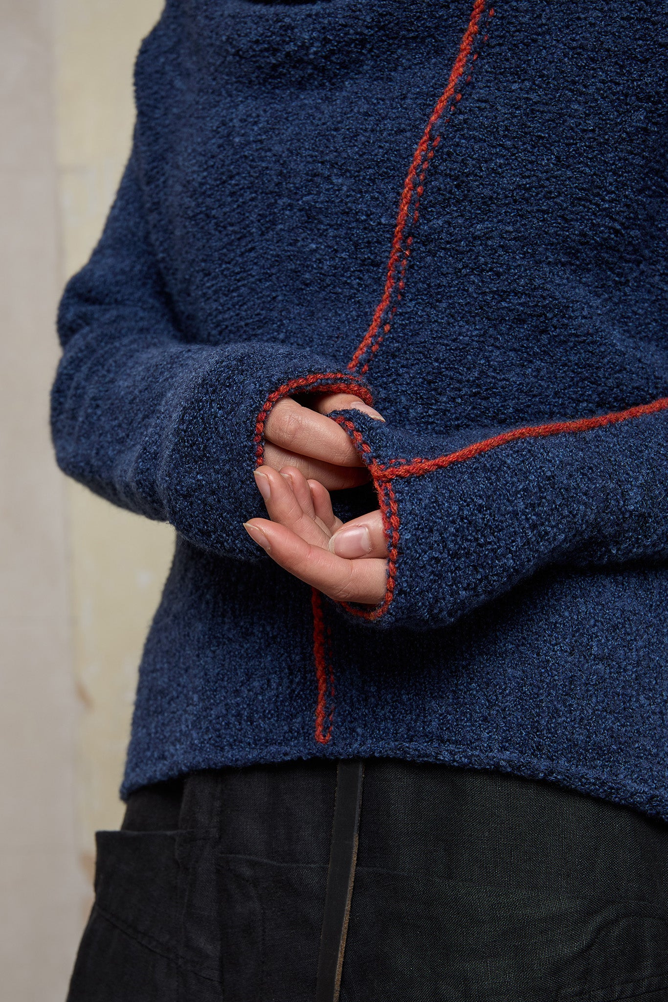 Close up fabric view of wool boucle knitted jumper in blue with orange external seams.