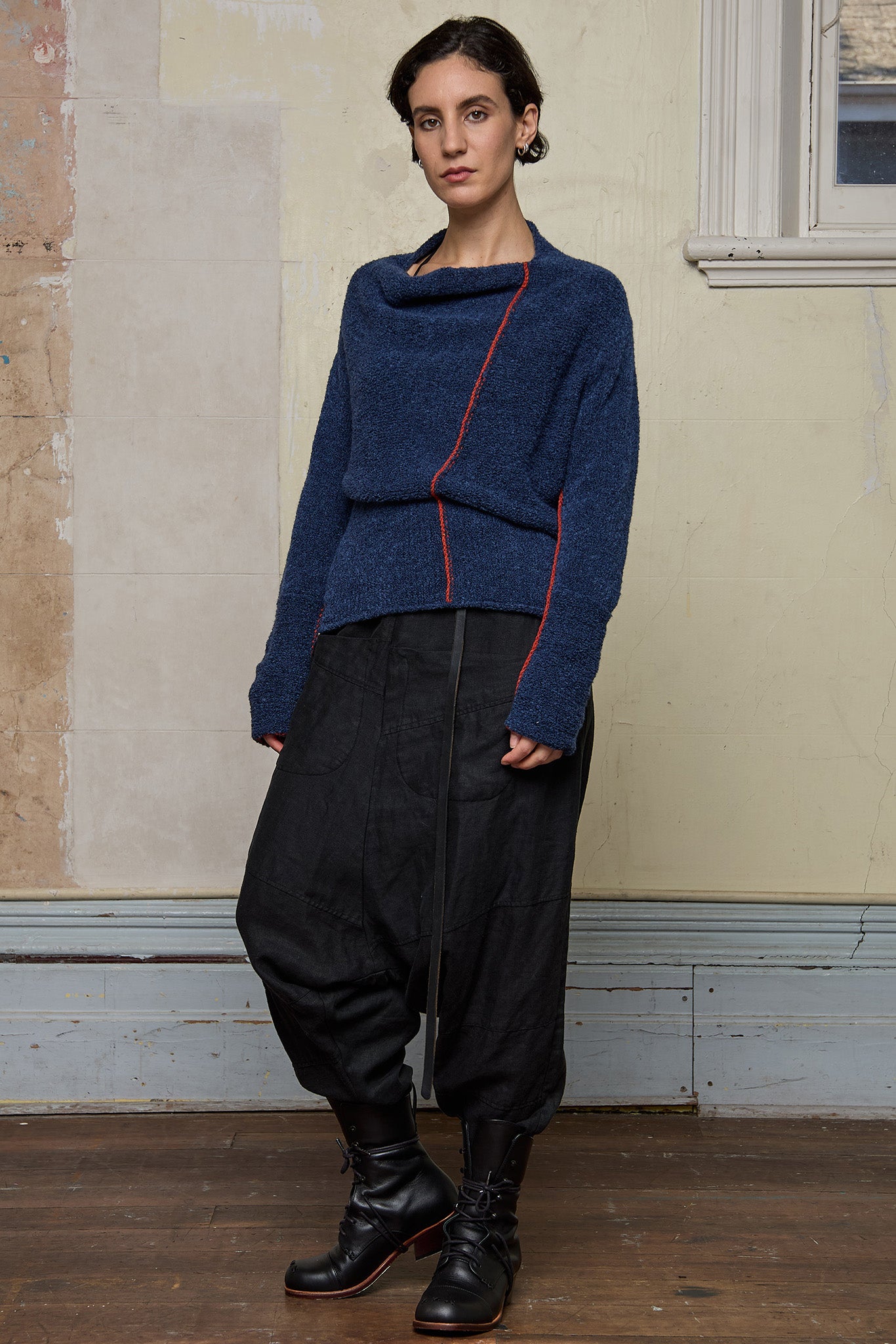 Front view of model wearing wool boucle knitted jumper in blue with orange external seams.