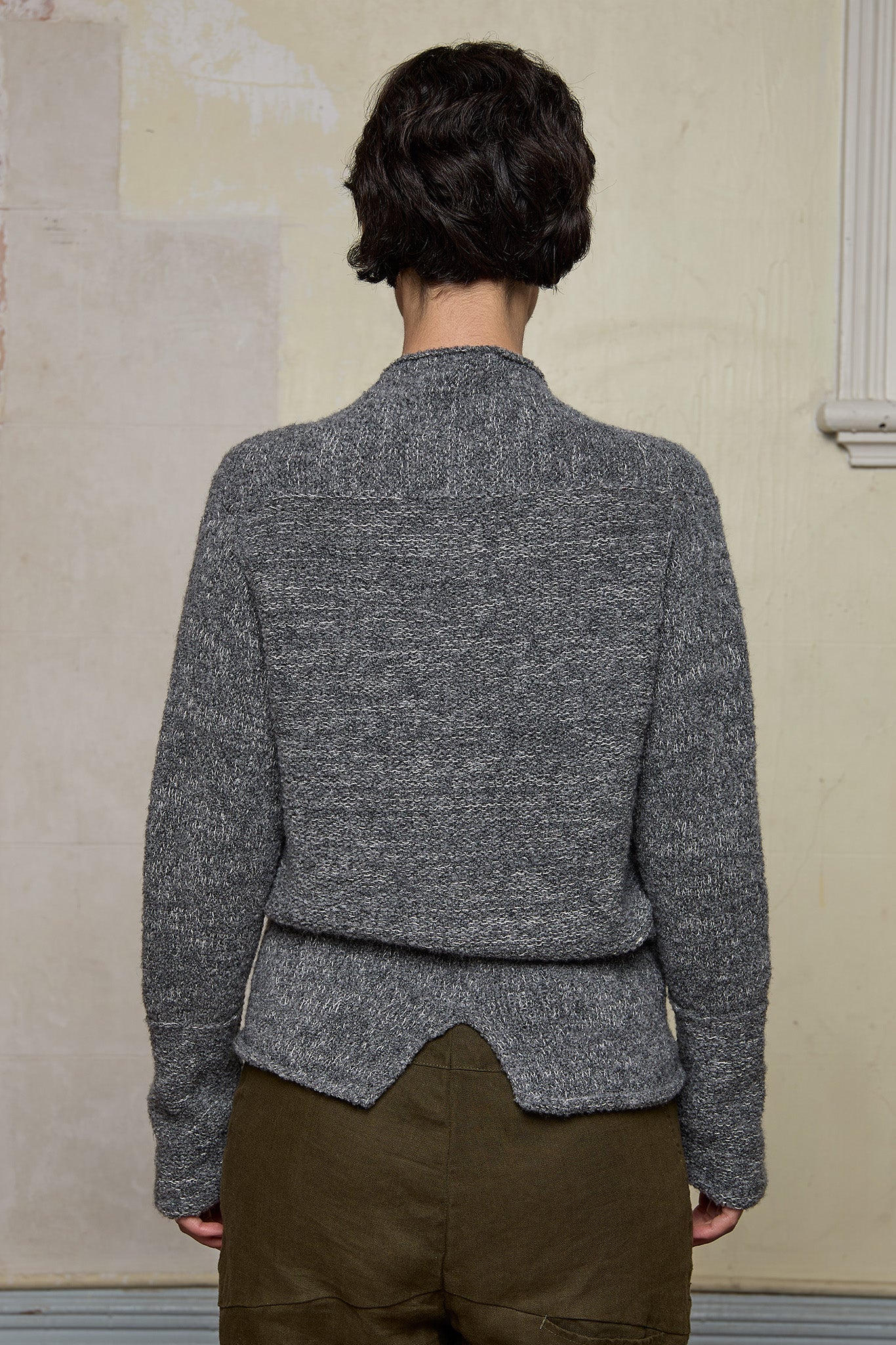 Back view of model wearing wool boucle knitted jumper in grey melange with decorative external seam details.