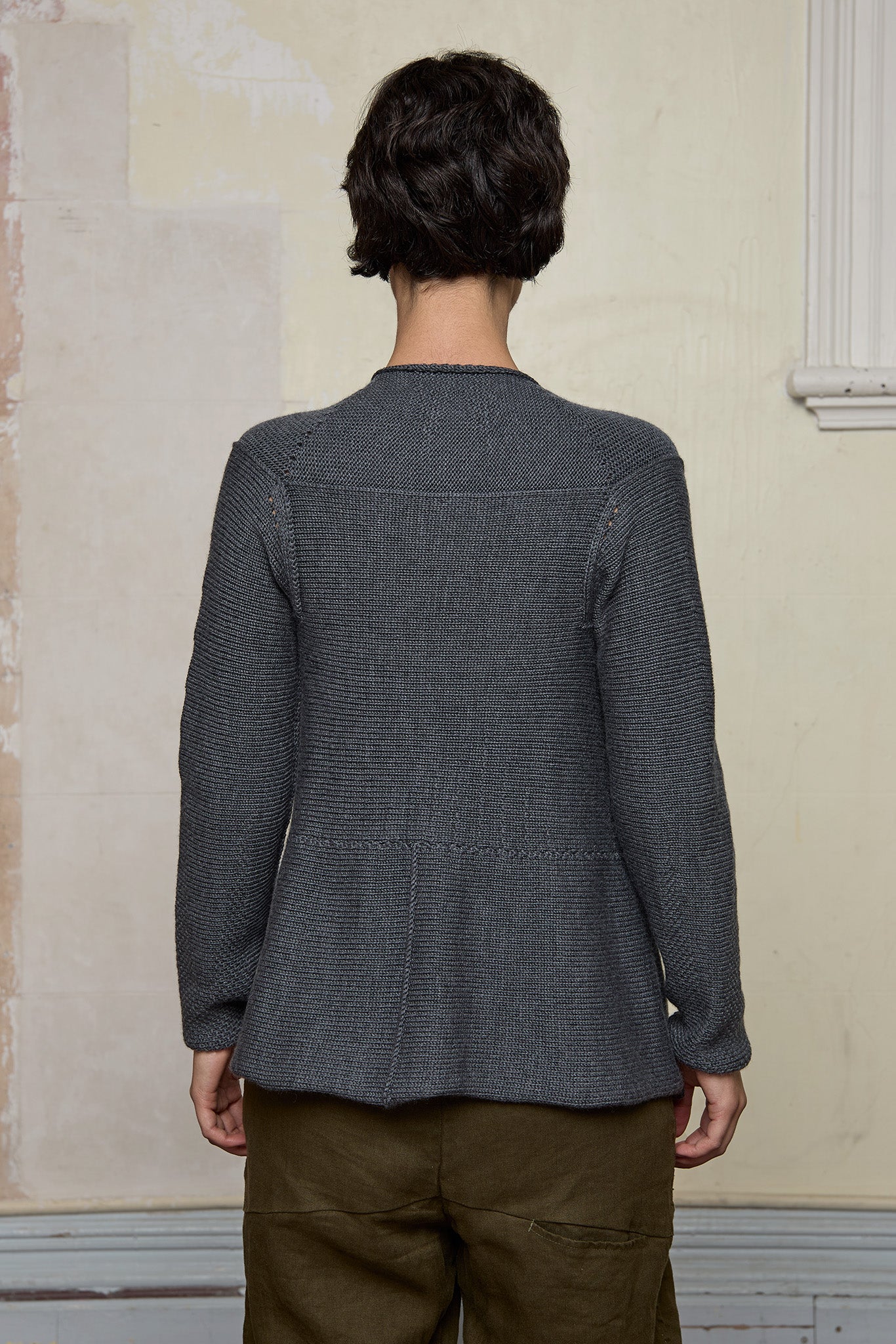 Back view of model wearing knitted peplum riding coat in steel grey, featuring vintage cloth covered buttons.  Made from superfine merino.