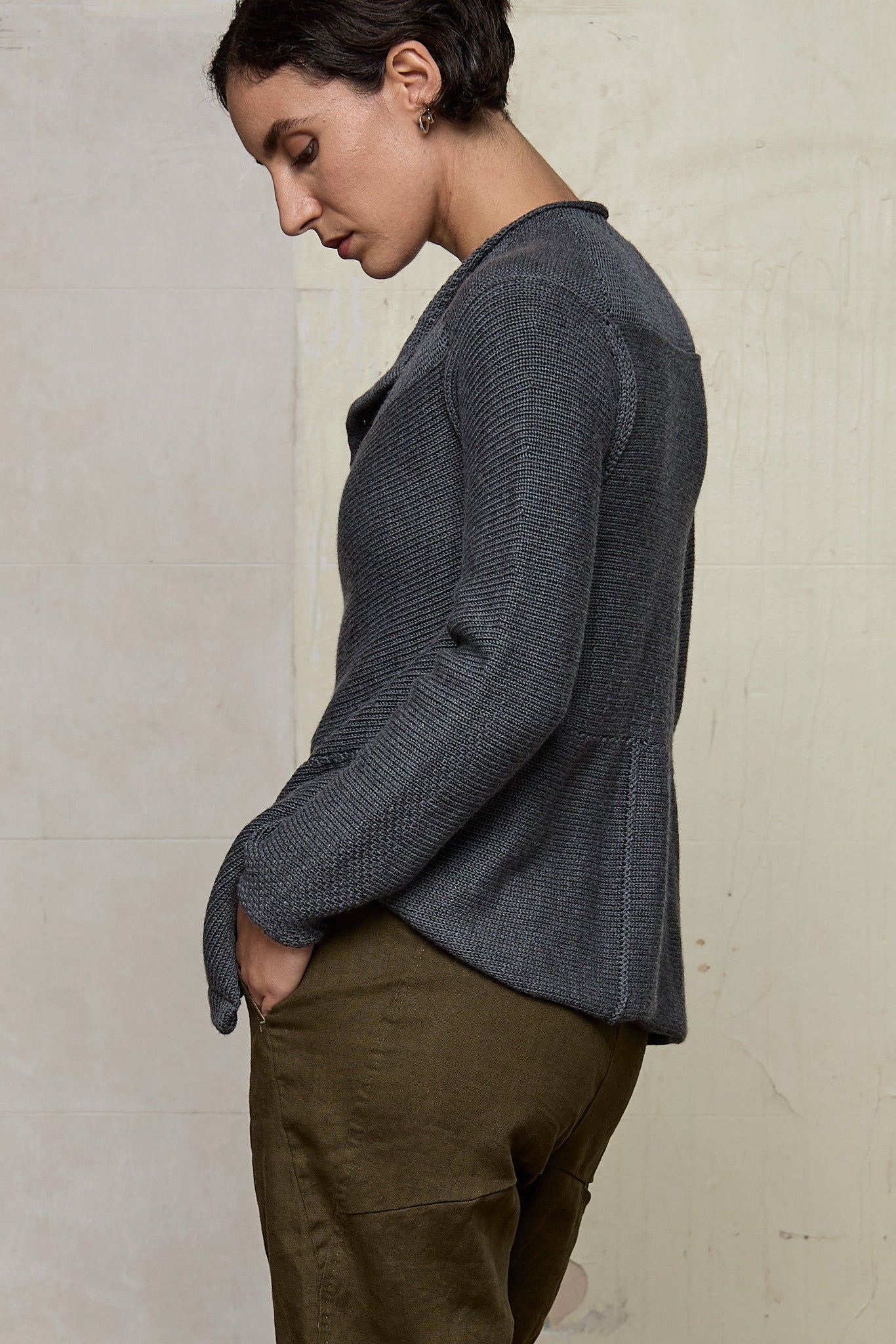 Side view of model wearing knitted peplum riding coat in steel grey, featuring vintage cloth covered buttons.  Made from superfine merino.