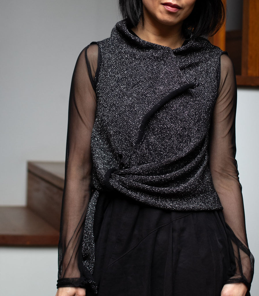 Model wears asymmetric self curling vest tied at waist, in a silver metallic backed with black merino wool fabric.