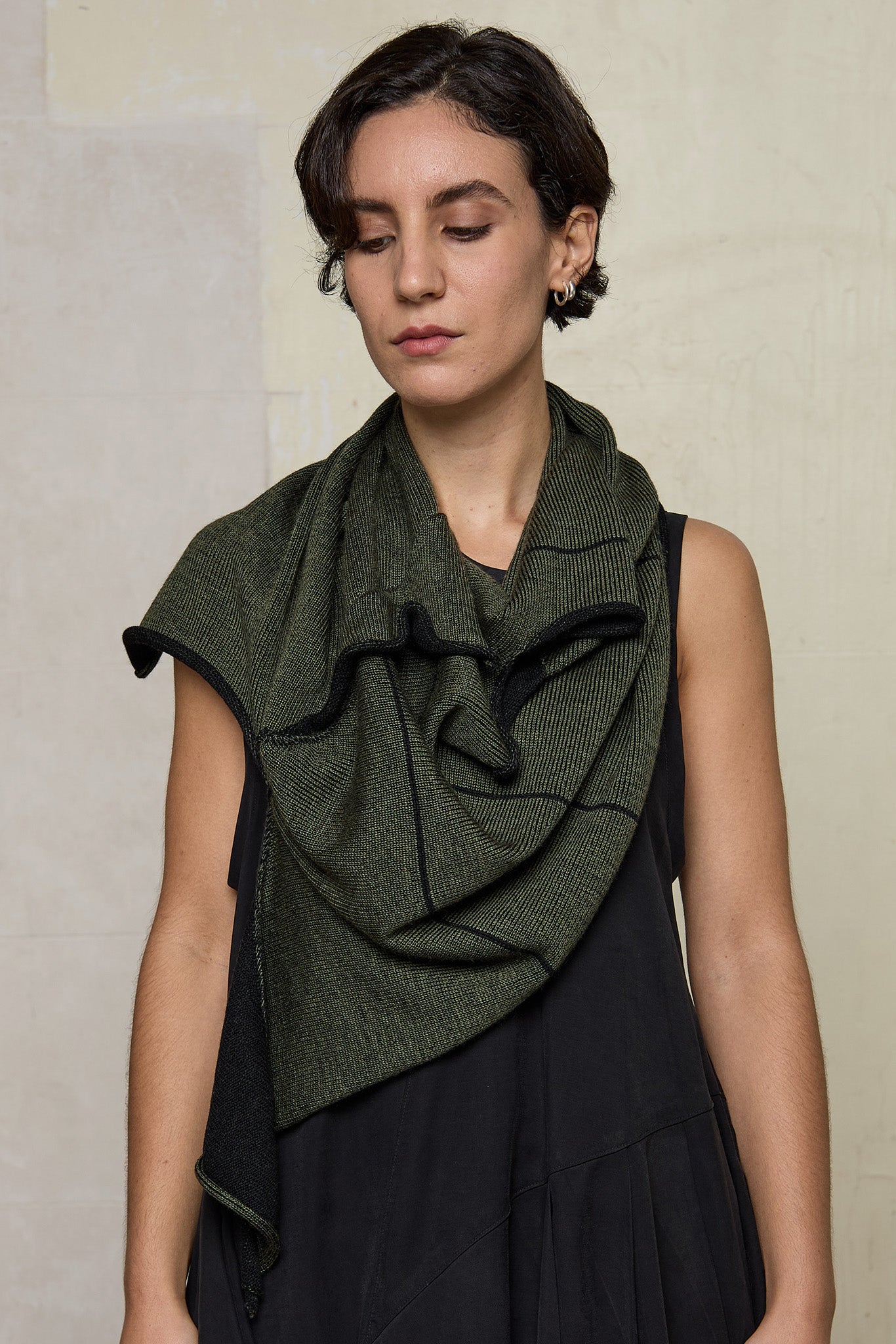 Model wears knitted asymmetric self-curling vest as a scarf, in army green on black colourway. Designed and knitted in Melbourne by Wendy Voon knits.