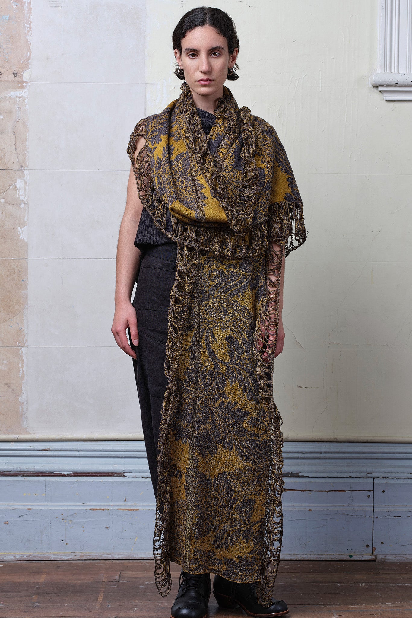 Model wears knitted damask scarf in a grey and gold colourway.