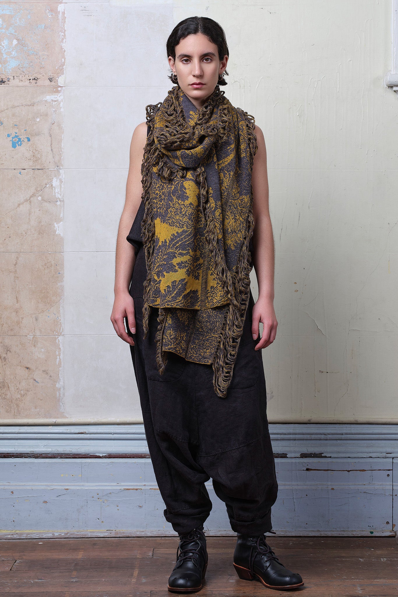 Model wears knitted damask scarf in a grey and gold colourway.