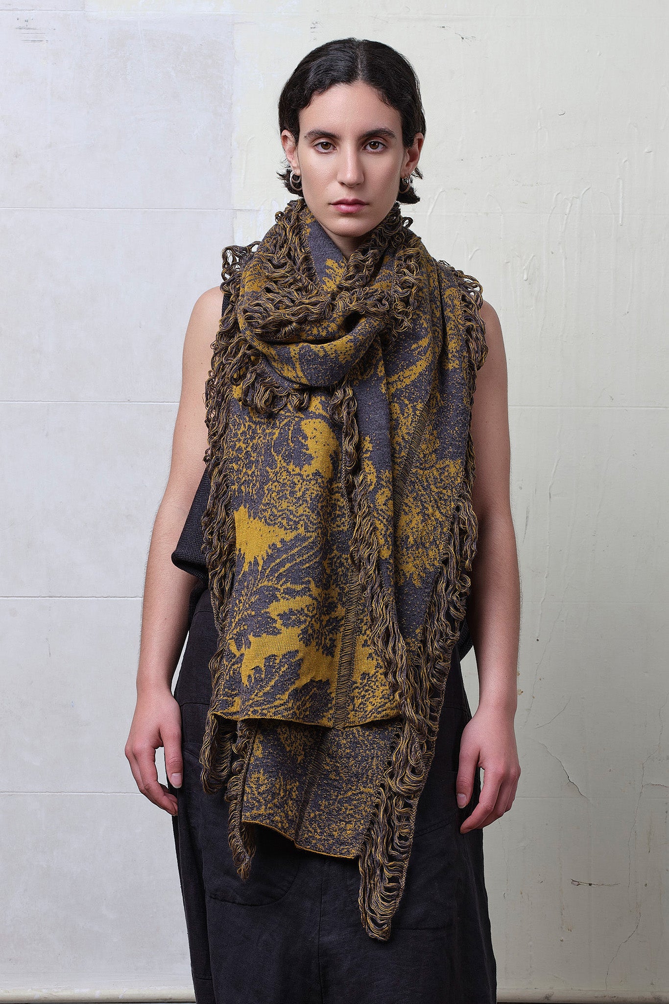Model wears knitted damask scarf in a grey and gold colourway.