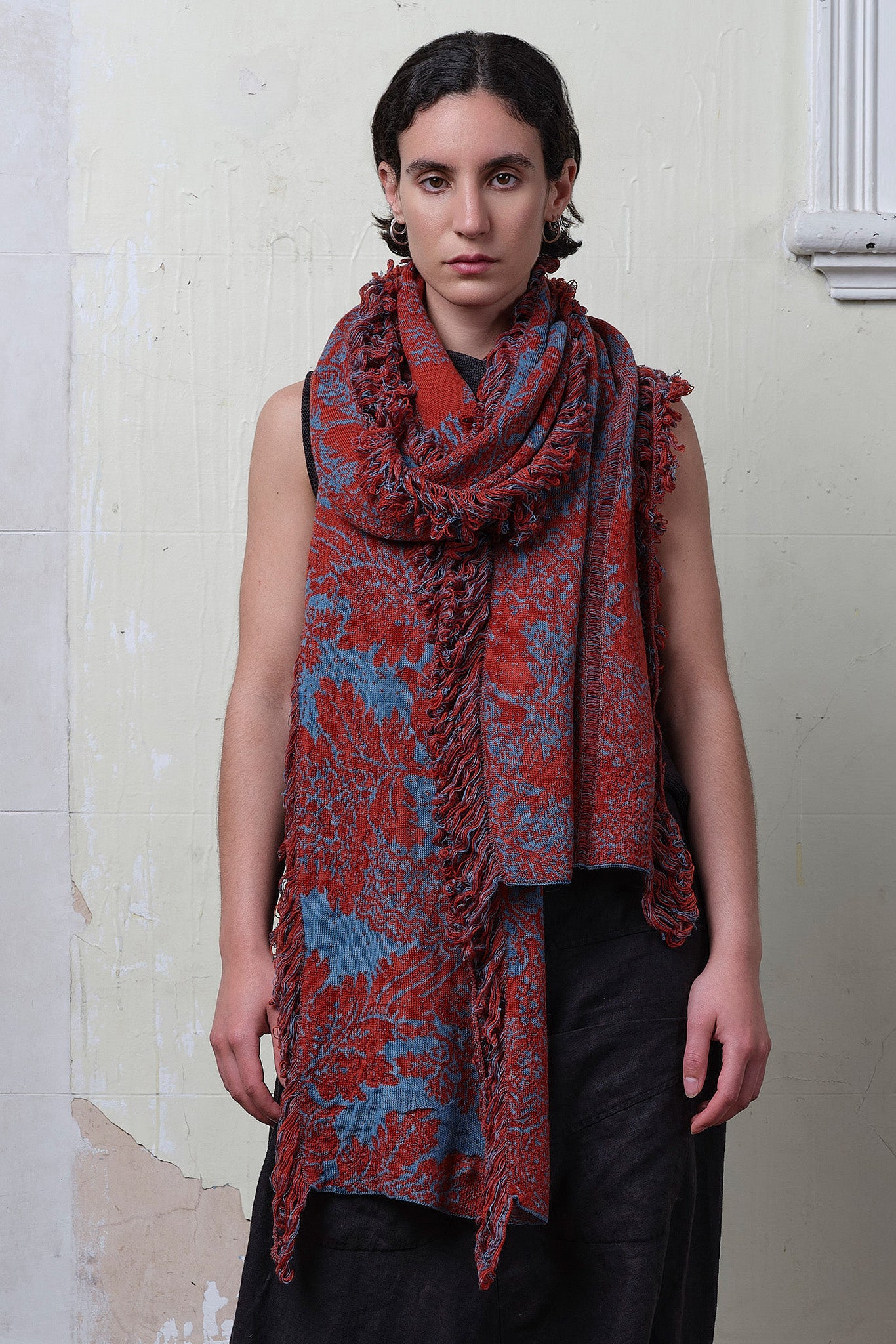 Model wears knitted wool/linen/cotton damask scarf in rust and lagoon blue colourway.