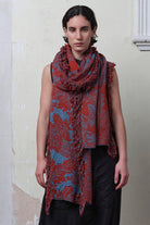 Model wears knitted wool/linen/cotton damask scarf in rust and lagoon blue colourway.