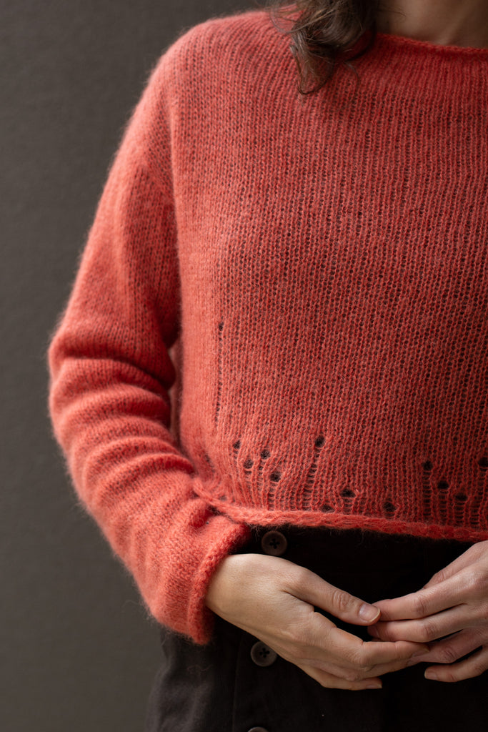 Close up of Front of super soft knitted jumper in a carrot colour way, featuring laddered laceholes, made from baby alpaca, mohair and silk. Designed and made in Melbourne by Wendy Voon knits