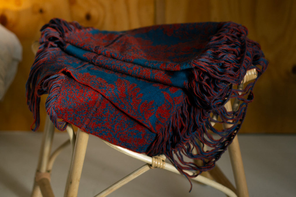 Wool rust and lagoon coloured damask patterned scarf, folded on a stool. Designed by Wendy Voon and made in Melbourne.