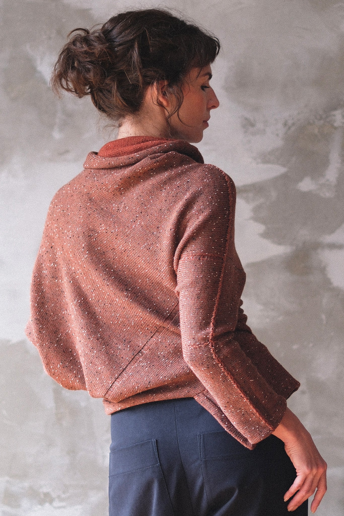 Back view of model wearing a wool bias knit jumper in terracotta flecked colourway. 