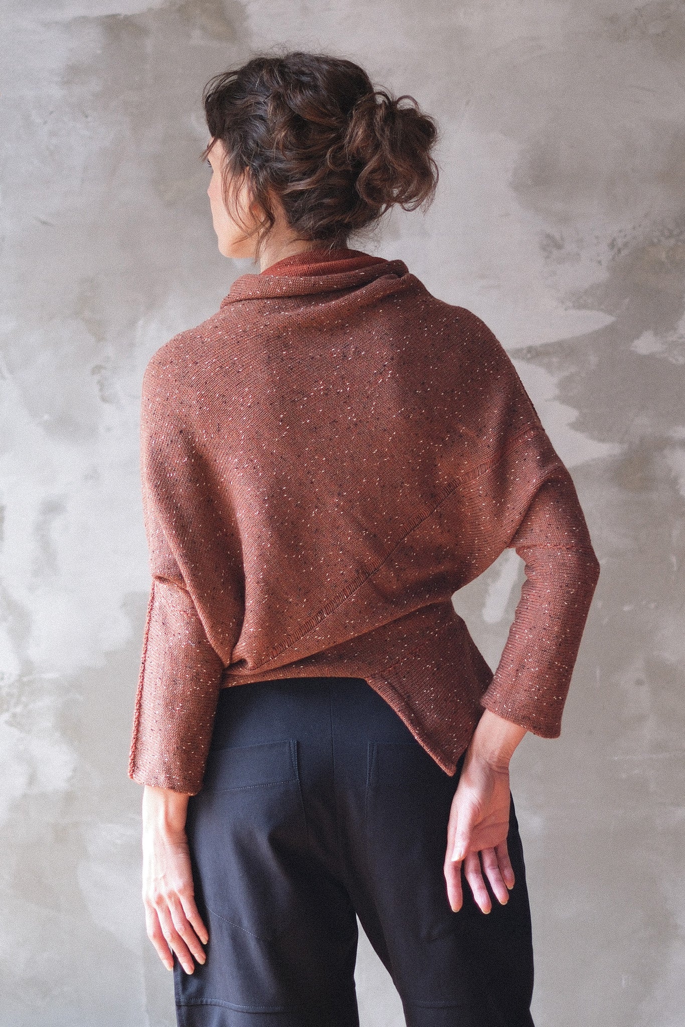 Back view of model wearing a wool bias knit jumper in terracotta flecked colourway. 