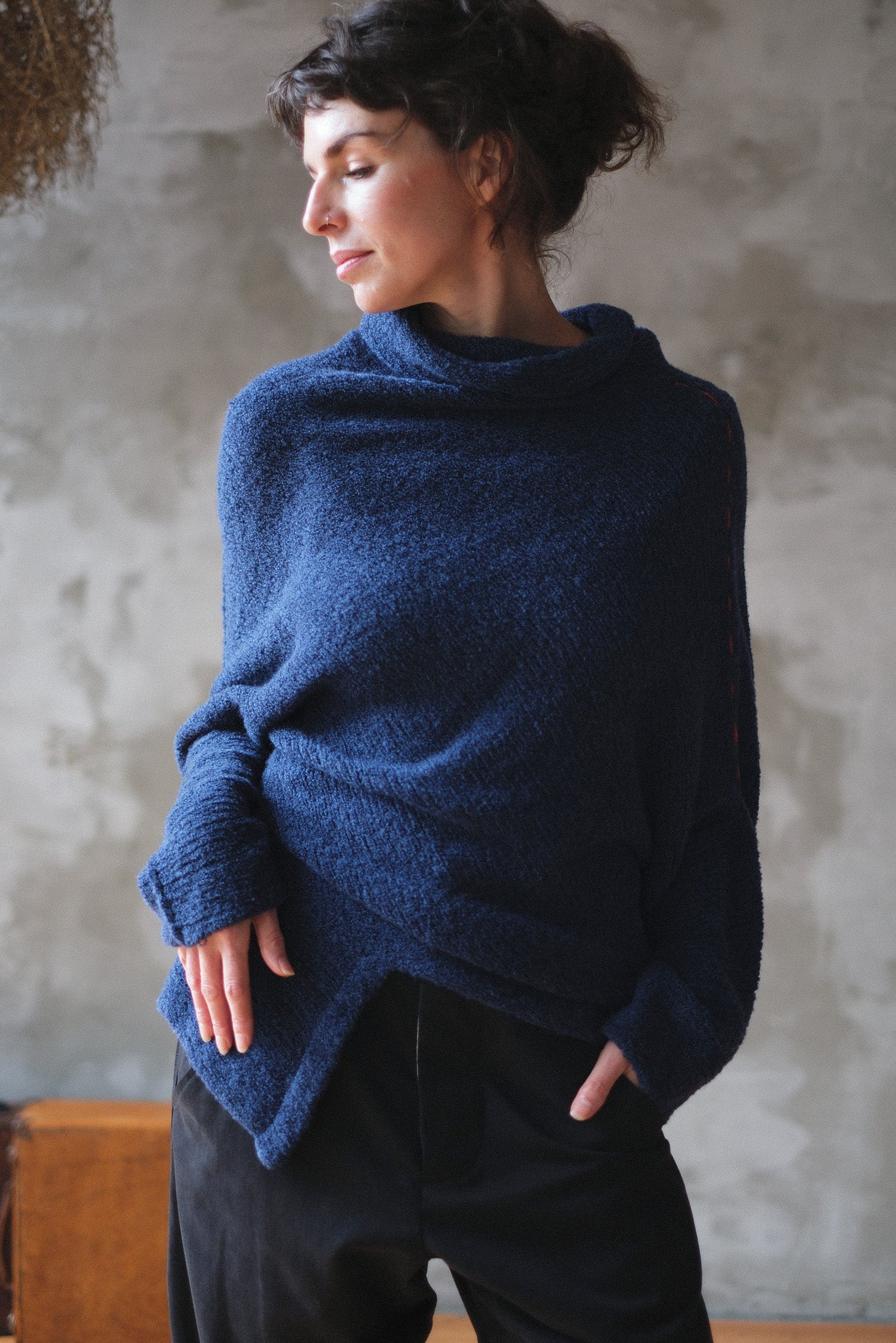 Woman wearing a blue knitted sweater with orange shoulder stitch detail against a textured wall.