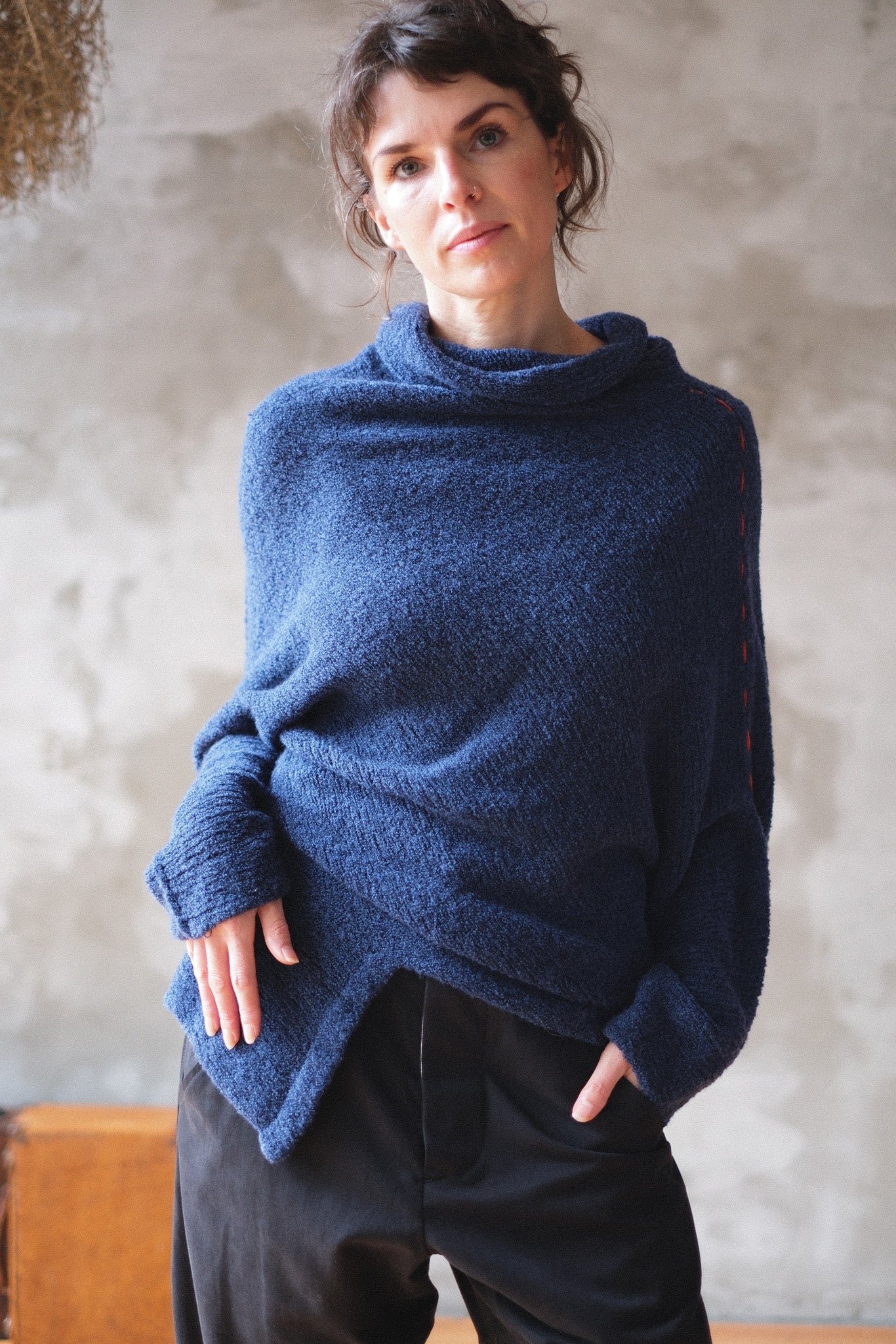 Woman wearing a blue knitted sweater with orange shoulder stitch detail against a textured wall.