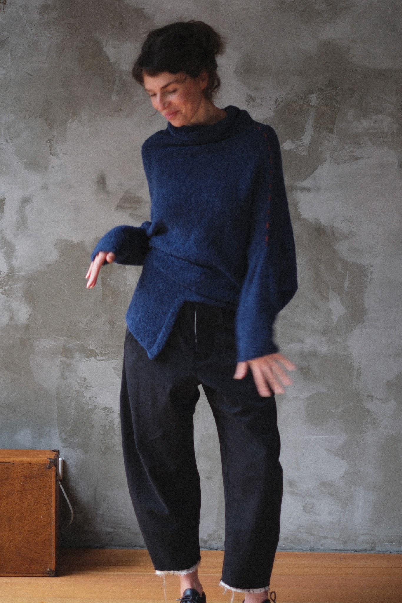 Woman wearing a blue knitted sweater with orange shoulder stitch detail against a textured wall.
