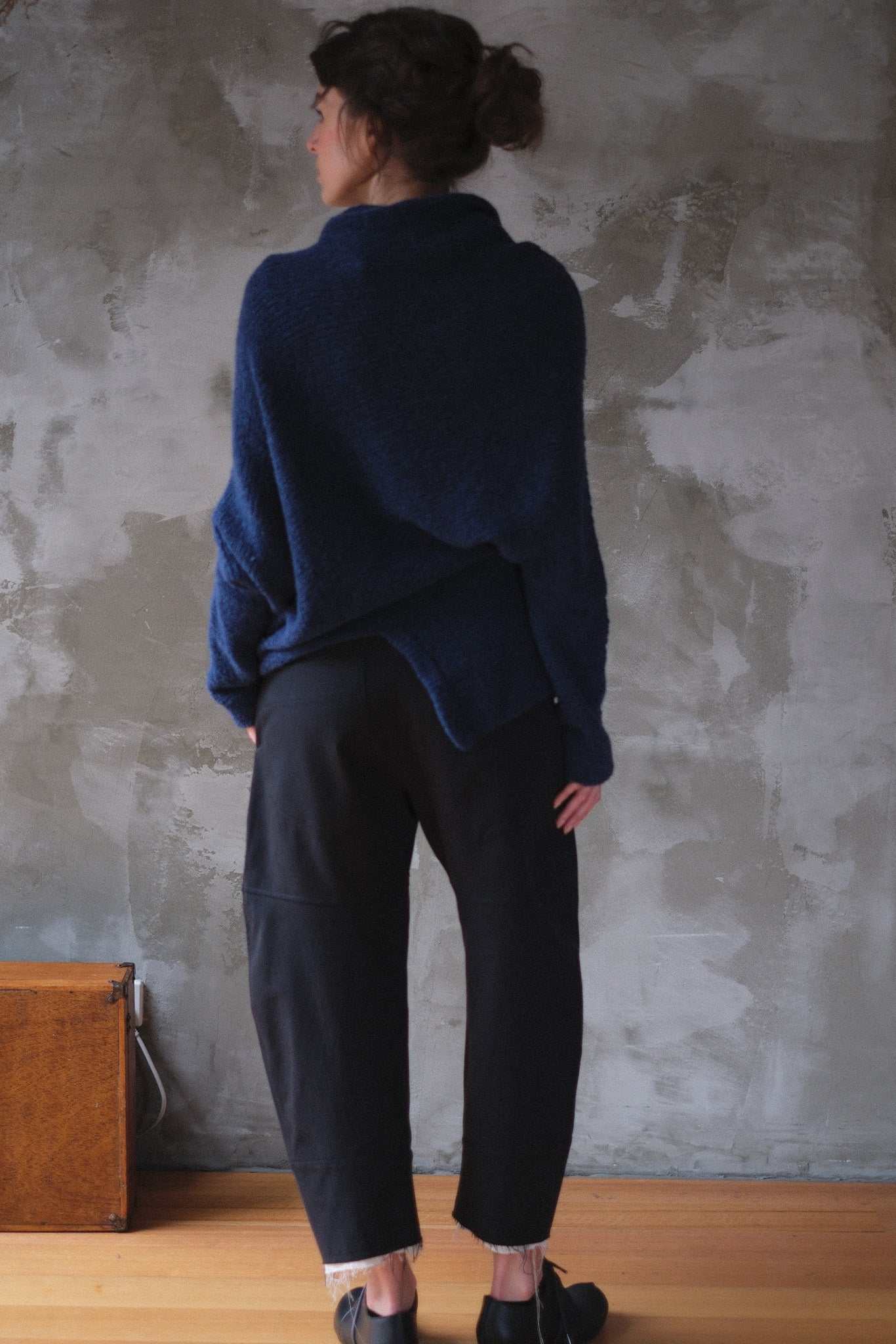 Woman wearing a blue knitted sweater with orange shoulder stitch detail against a textured wall.