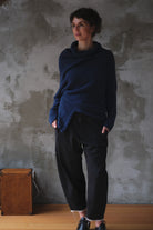Woman wearing a blue knitted sweater with orange shoulder stitch detail against a textured wall.