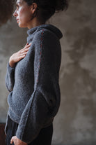 Woman wearing a textured gray sweater with orange shoulder seam detail against a neutral background