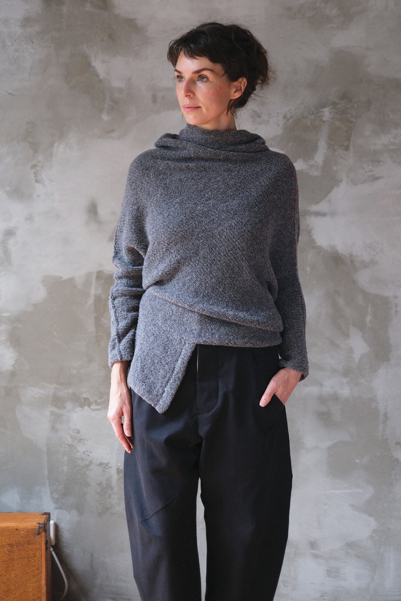 Woman wearing a textured gray sweater with orange shoulder seam detail against a neutral background