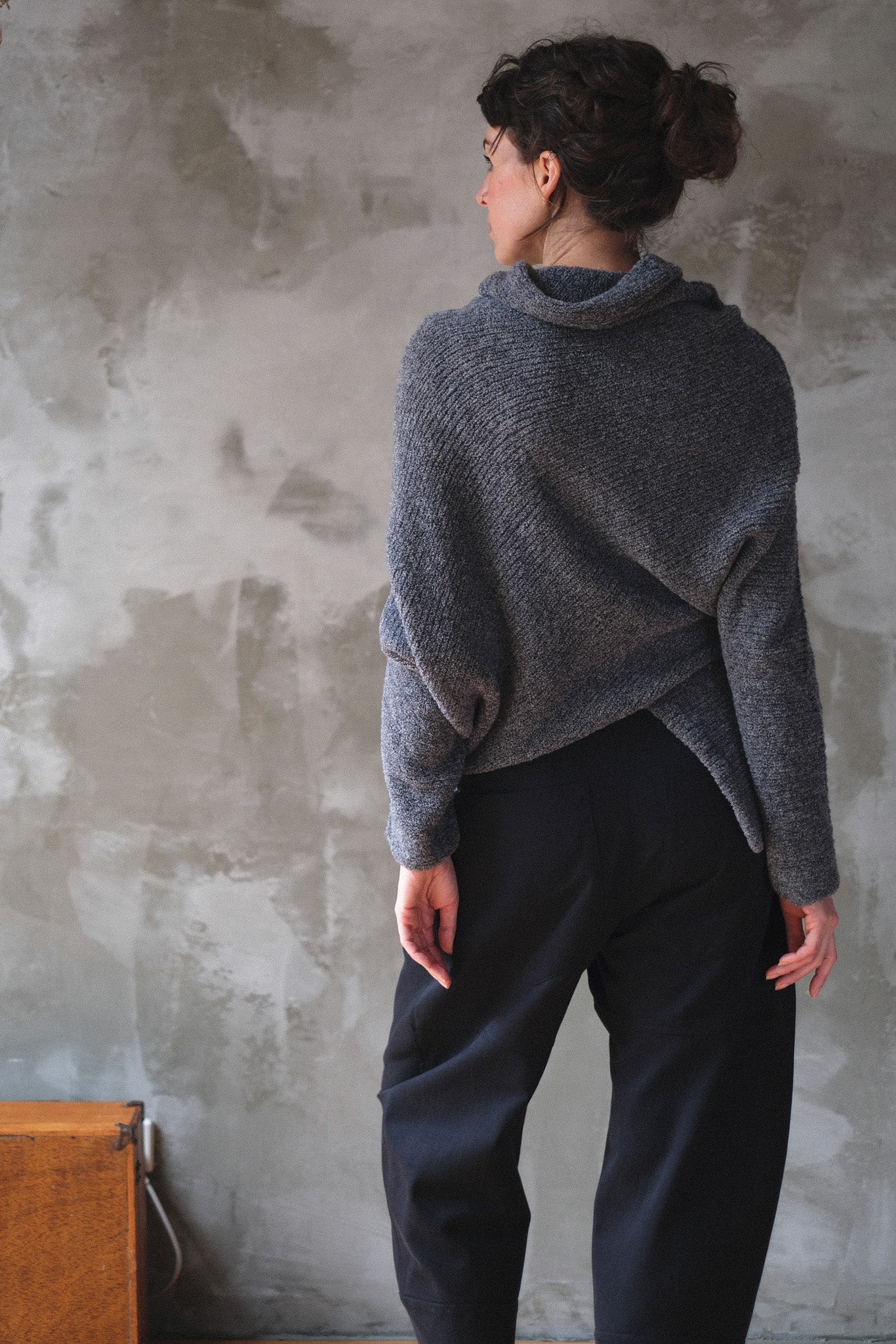 Woman wearing a textured gray sweater with orange shoulder seam detail against a neutral background