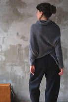 Woman wearing a textured gray sweater with orange shoulder seam detail against a neutral background