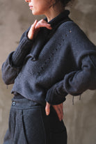 A close-up of a person wearing a charcoal gray knit sweater with lacehole details and ruching on sleeves.