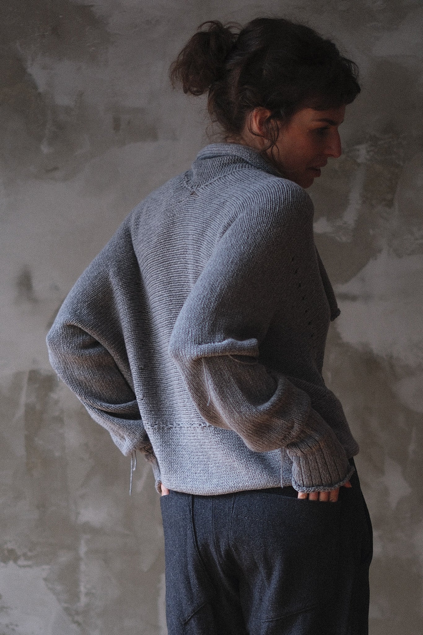 Back view of model wearing a soft grey chunky knit cropped cardigan with a shawl collar and ruched sleeve detail.