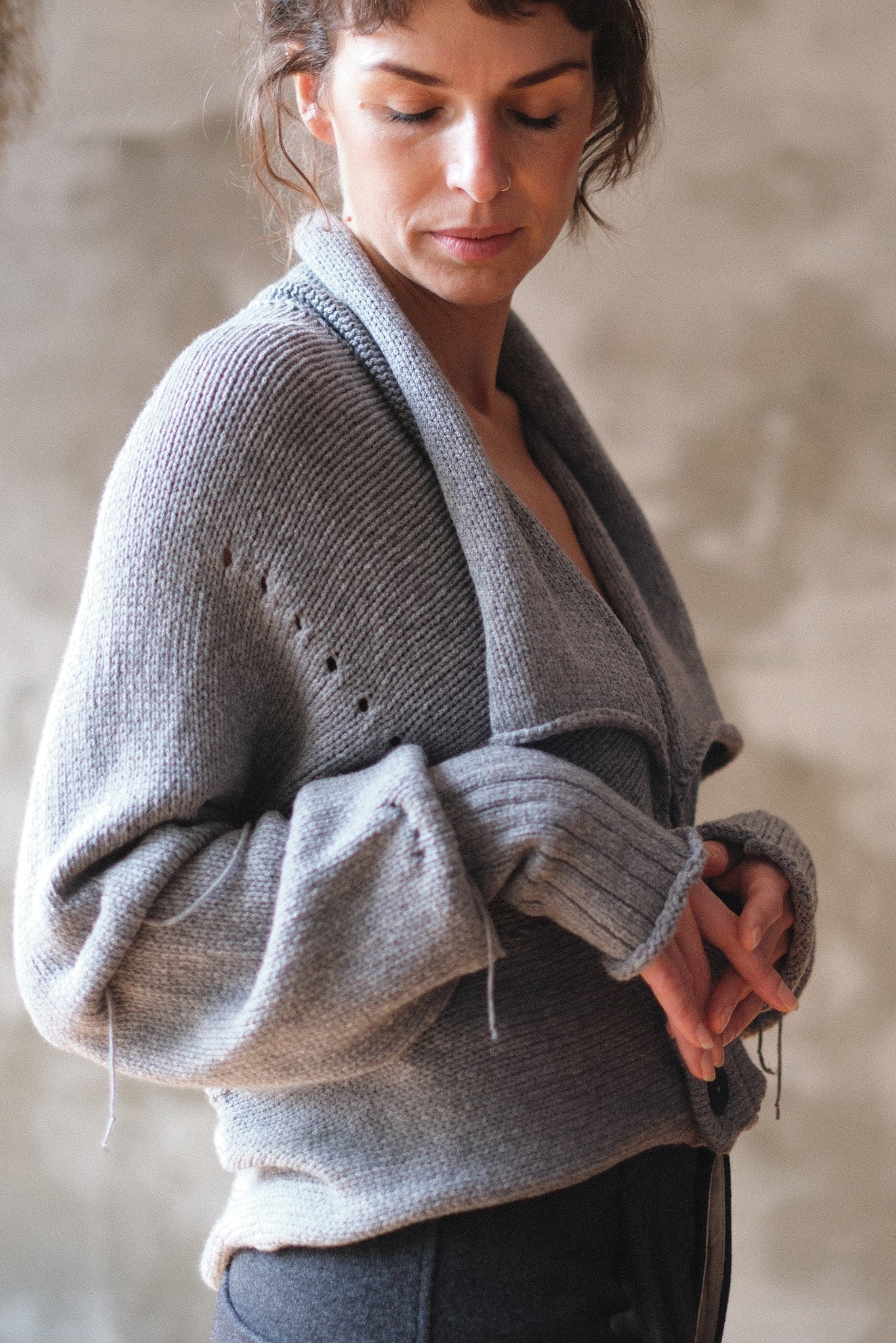 Models wears a soft grey chunky knit cropped cardigan with a shawl collar and ruched sleeve detail.