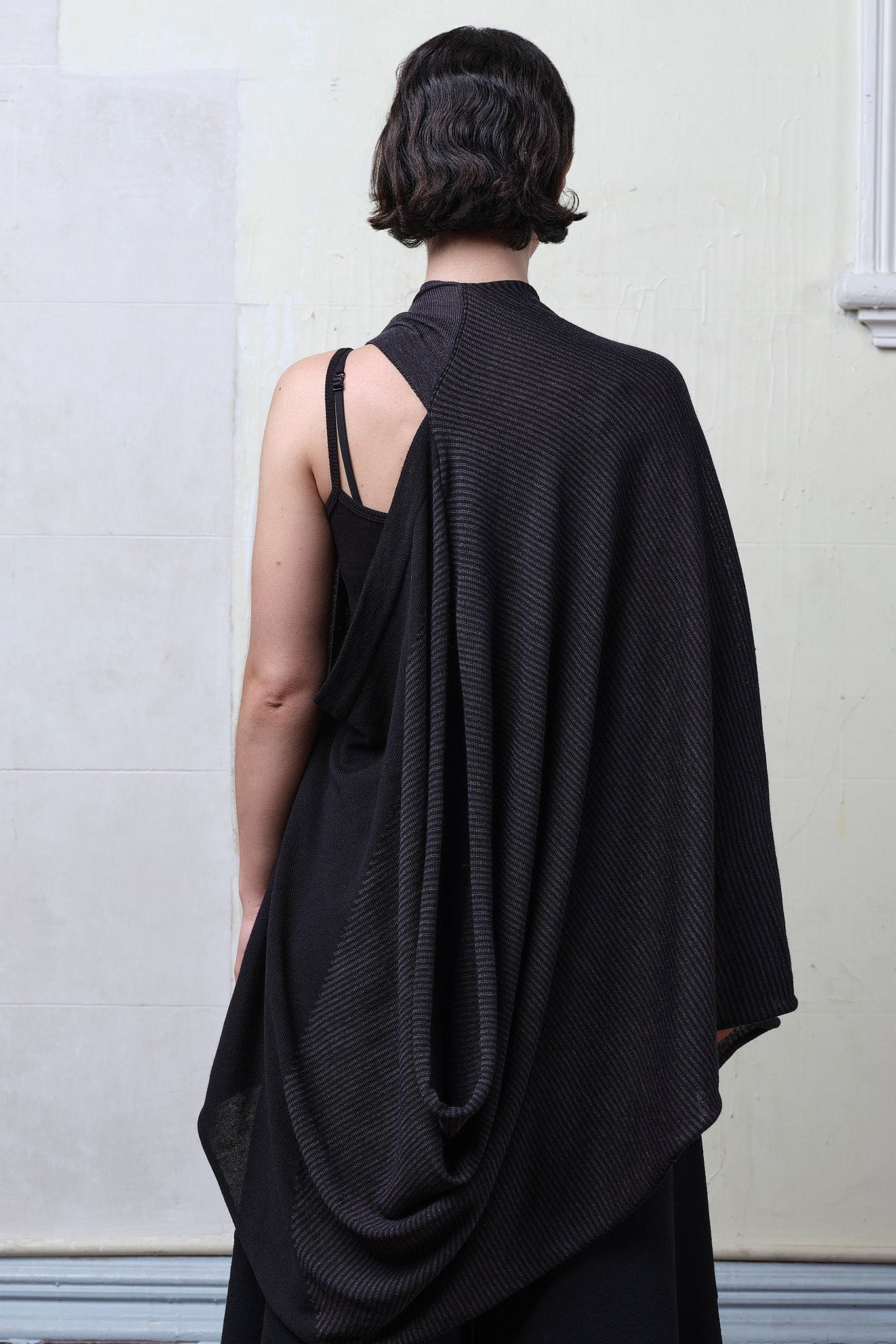 Back view of model wearing a wool striped wrap, with head through armhole, and arm through neckline, in charcoal/black colourway. Designed and made in Melbourne by Wendy Voon knits.