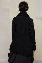 Model wears black knitted coat upside down, made from alpaca and superfine merino wool.