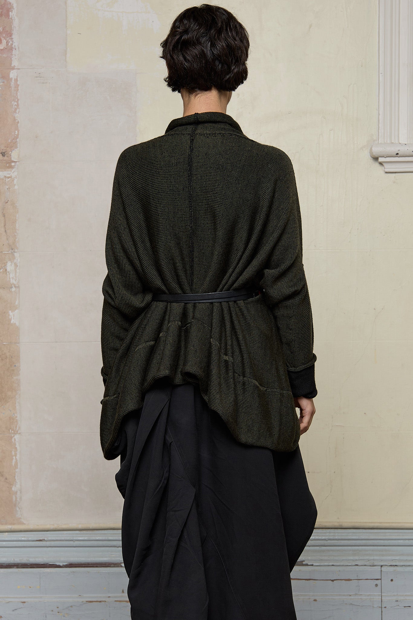 Back view of box shaped jumper, worn belted.  Designed by Wendy Voon, in an army with black backed fabric, made from superfine merino wool.
