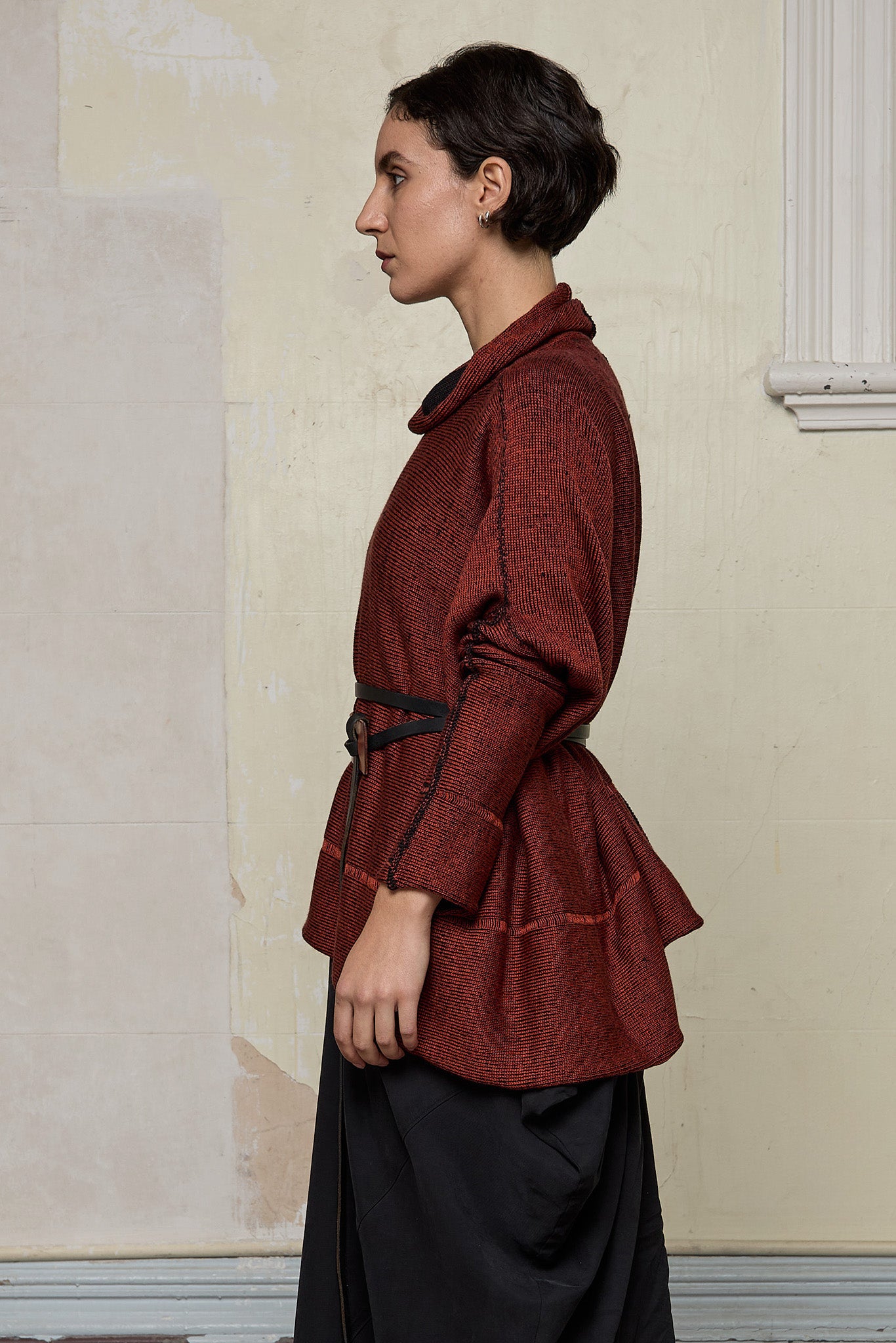 Side view of box shaped jumper designed by Wendy Voon, in a vermillion with black backed fabric, worn belted. Made from superfine merino wool.