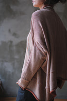 A person shown from the side wearing a loose, draped knit jumper with fawn and terracotta melange colourway (terracotta jumper worn inside out).