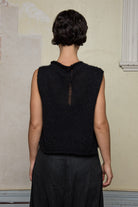 Back view of model wearing a super lush knitted vest in black. Vest features random laceholes along hemline.